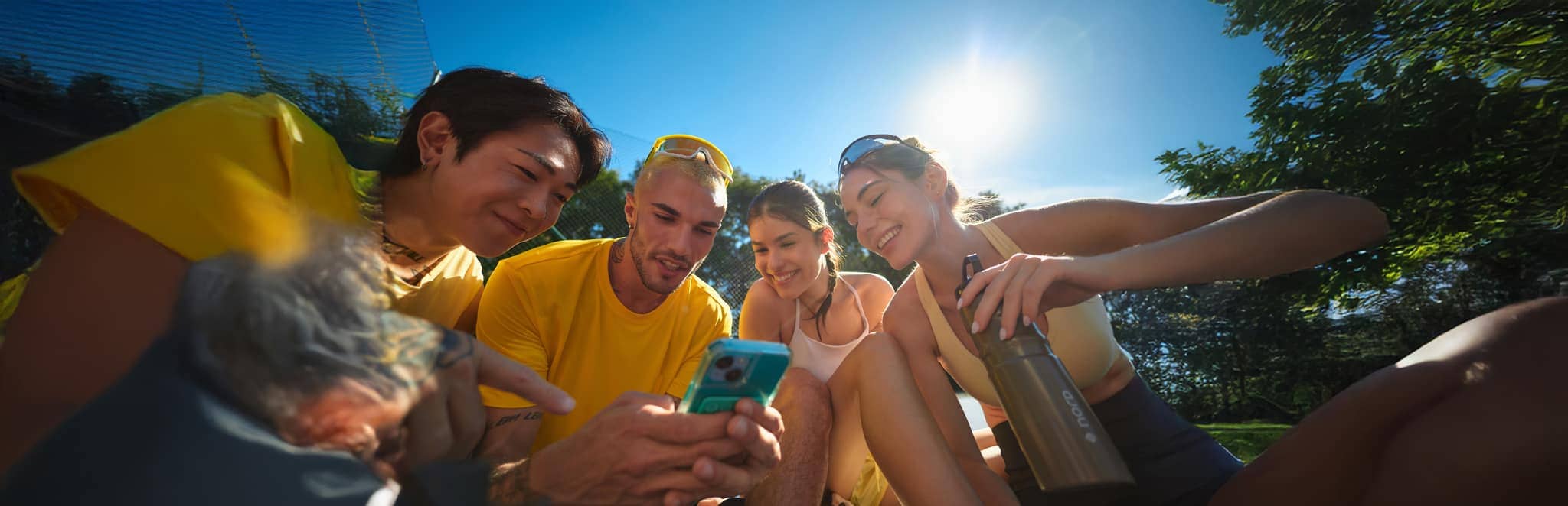 Grupo de amigos sorrindo e usando o celular ao ar livre