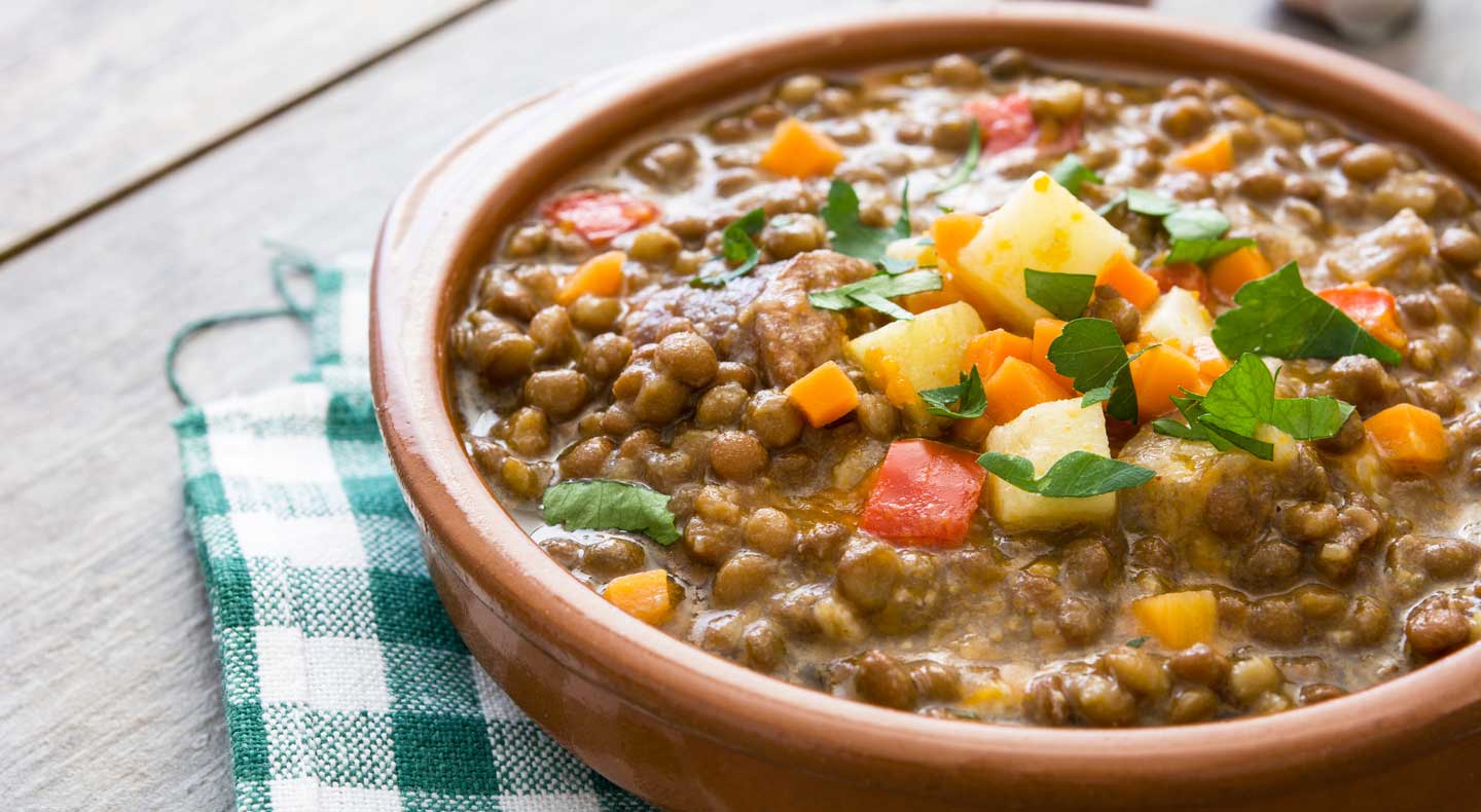 Sopa de lentilha servida em tigela de barro, sobre jogo americano quadriculado