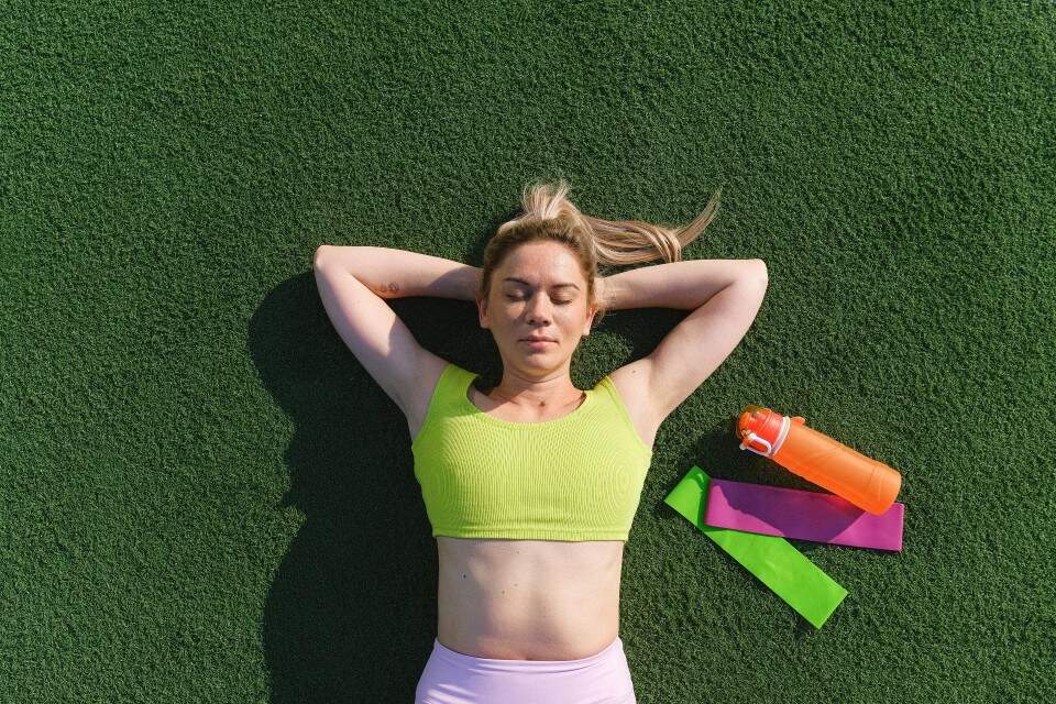 Mulher com roupas próprias para exercício deitada em um gramado com expressão relaxada
