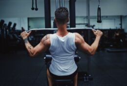 Imagem mostra homem em ambiente de academia praticando puxada alta