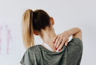 Imagem mostra mulher em roupas de academia, tocando o próprio pescoço, como se estivesse com dor nas costas