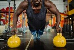 Homem se exercita com kettlebells em ambiente de academia