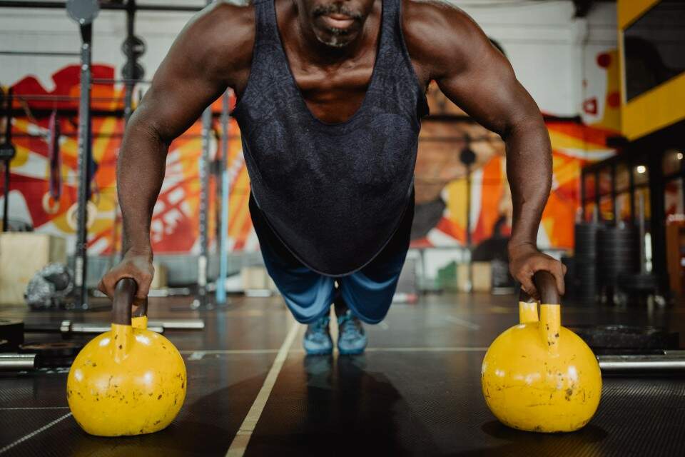 Homem se exercita com kettlebells em ambiente de academia