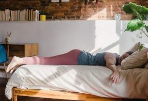 Imagem mostra mulher em roupas de ginástica deitada em uma cama, visivelmente cansada, mas sorrindo