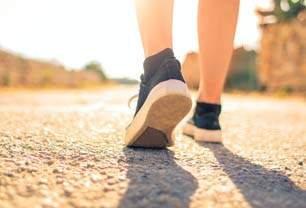 Imagem mostra pés calçados de tênis esportivos, caminhando no asfalto