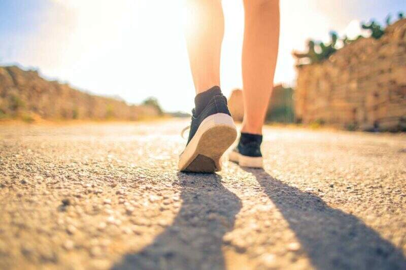 Imagem mostra pés calçados de tênis esportivos, caminhando no asfalto