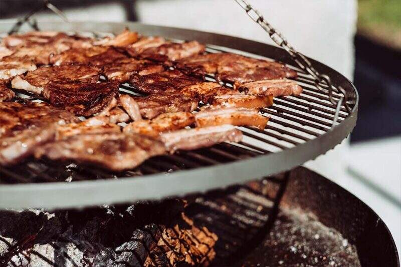 Imagem mostra carnes sendo preparadas em uma grelha sobre carvão