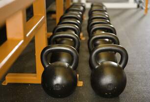 Imagem exibe fila de kettlebells em ambiente de academia