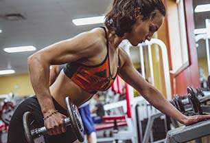 Imagem mostra mulher musculosa levantando peso em ambiente de academia