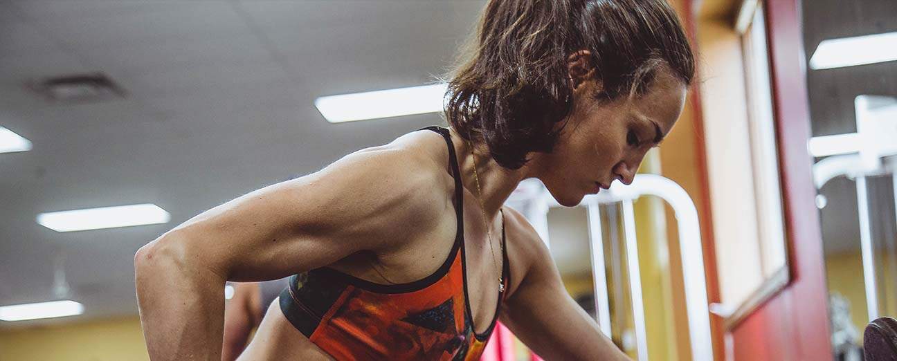 Imagem mostra mulher musculosa levantando peso em ambiente de academia