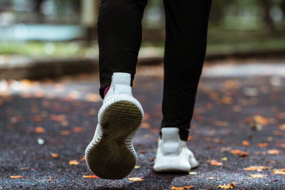 Imagem mostra apenas pés calçados com tênis esportivos, correndo no asfalto