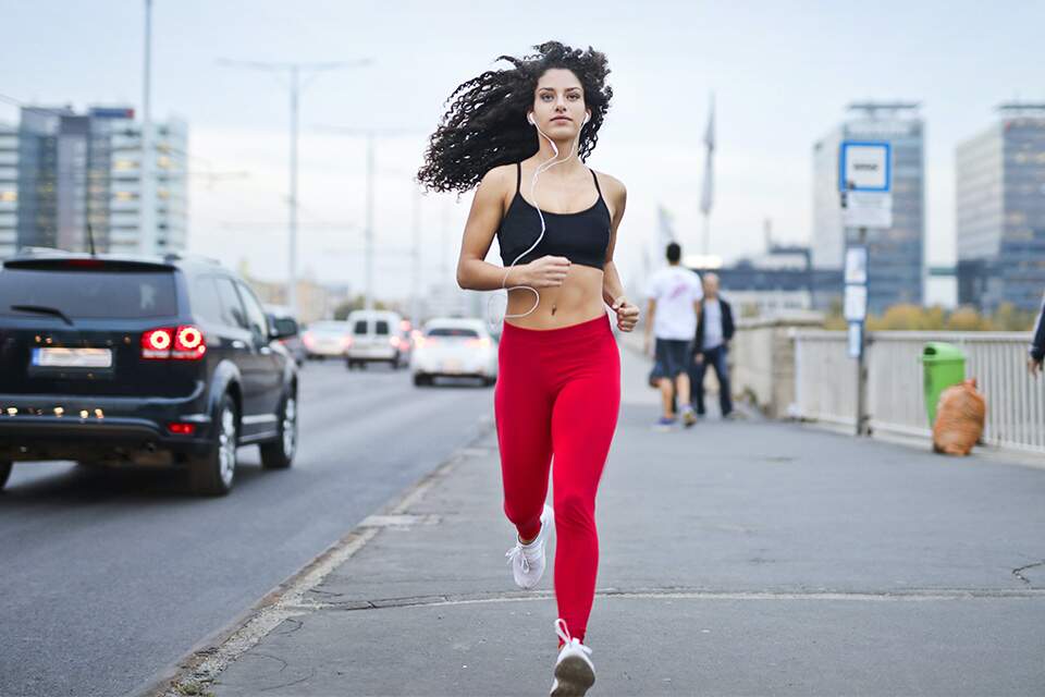 Imagem mostra mulher de fones de ouvido praticando corrida na rua