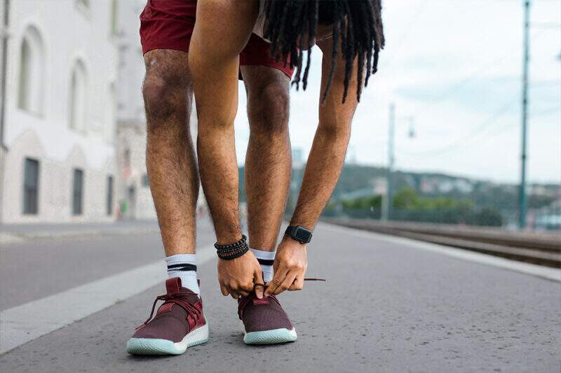 Imagem mostra homem em trajes de corrida ajustando os tênis