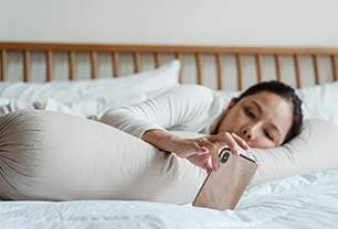 Imagem mostra mulher na cama olhando um celular
