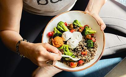 Imagem mostra mulher em roupas de treino comendo em um prato de comida natural de muitas variedades e cores