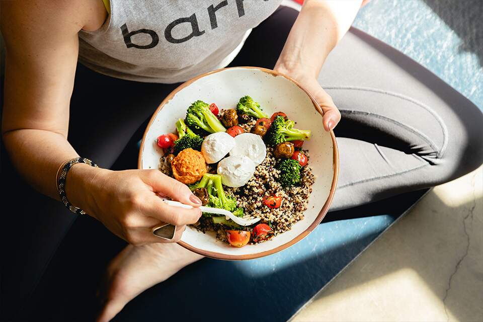 Imagem mostra mulher em roupas de treino comendo em um prato de comida natural de muitas variedades e cores