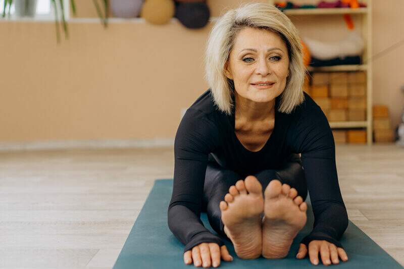 Imagem mostra mulher de meia idade fazendo um exercício de alongamento