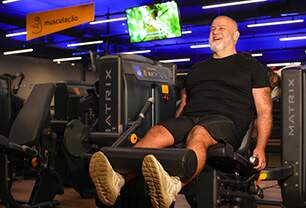 Imagem mostra homem em ambiente de academia, treinando o joelho em um aparelho
