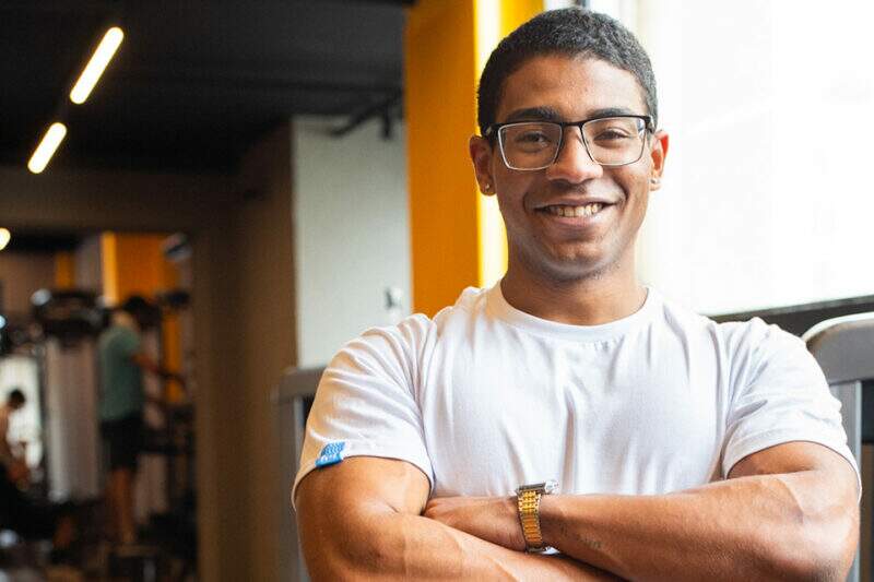 Aluno em ambiente de academia, sorrindo para a foto