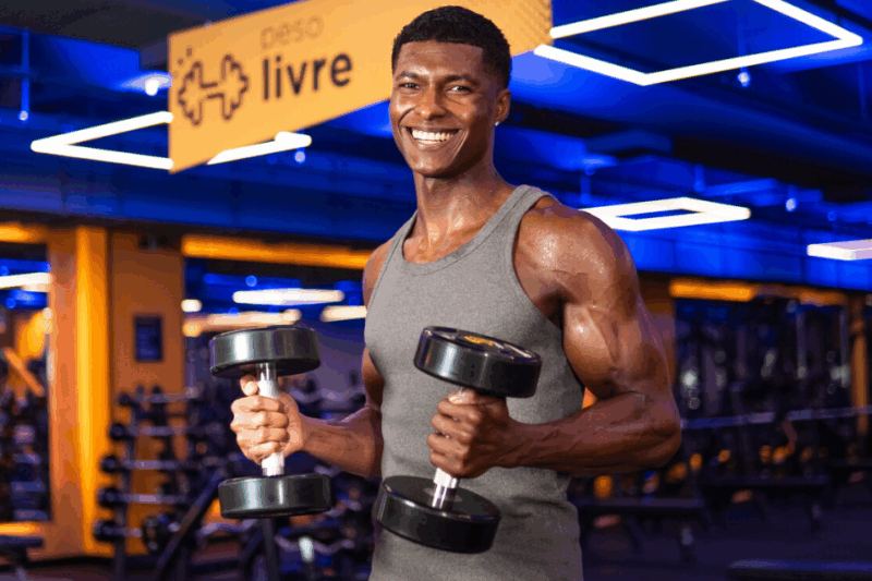 Homem segurando halters e sorrindo em uma unidade da Smart Fit.