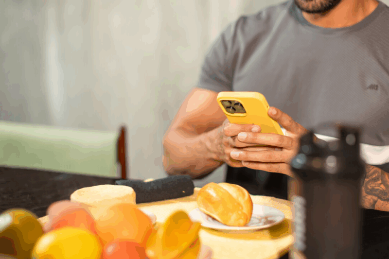 Pessoa mexendo no celular de frente para frutas e pão.