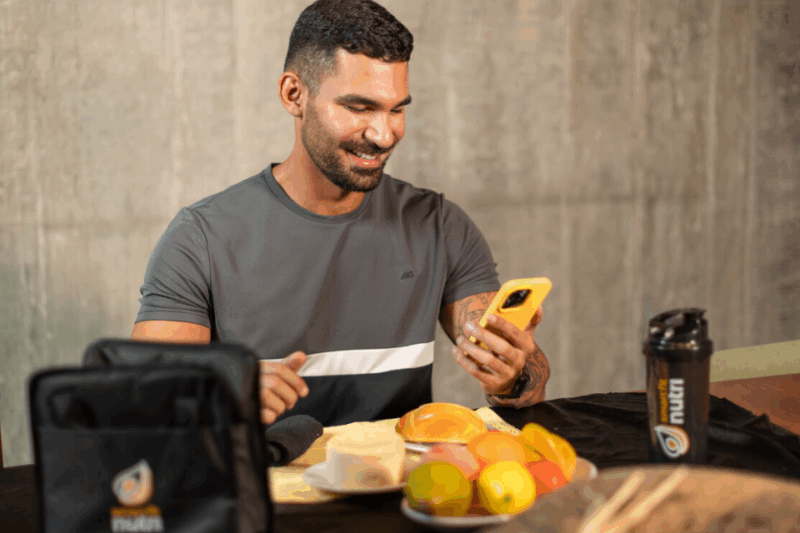 pessoa mexendo no celular com pão e frutas a sua frente