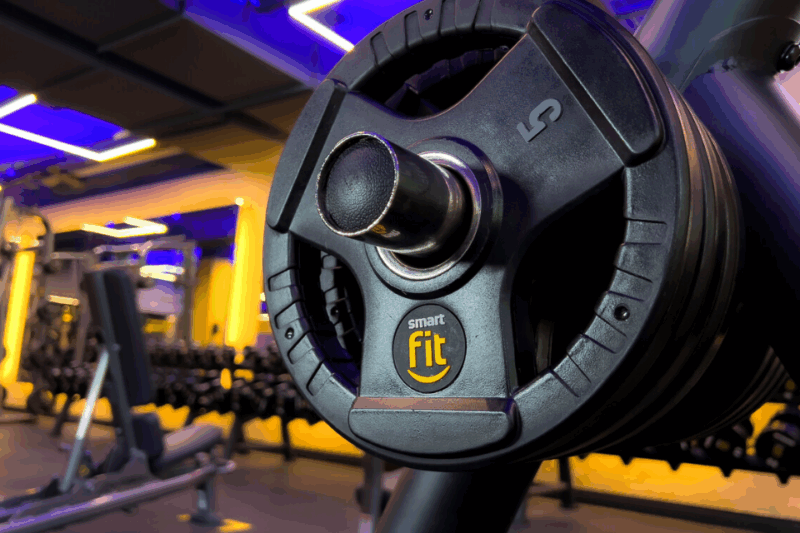 A imagem apresenta uma fileira de pesos de 5 kg da Smart Fit.