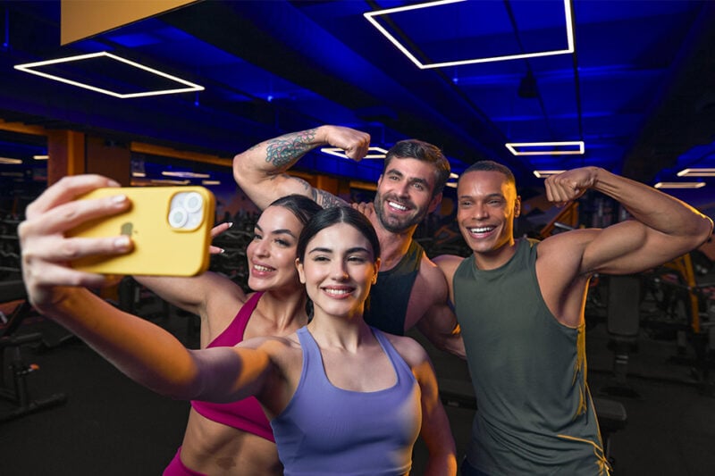 Grupo de amigos tirando selfie na academia Smart Fit, sorrindo e fazendo pose após o treino em ambiente moderno e iluminado.