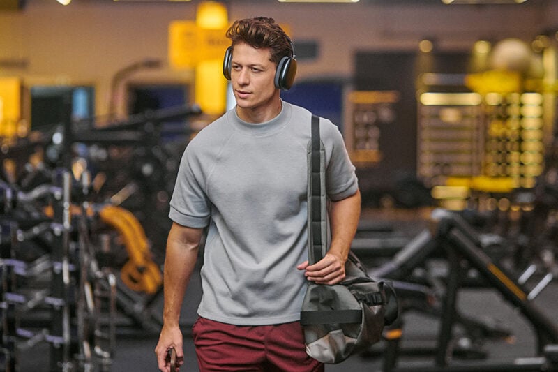 Pessoa caminhando pela academia Smart Fit com fones de ouvido e bolsa de treino, em ambiente amplo e iluminado.