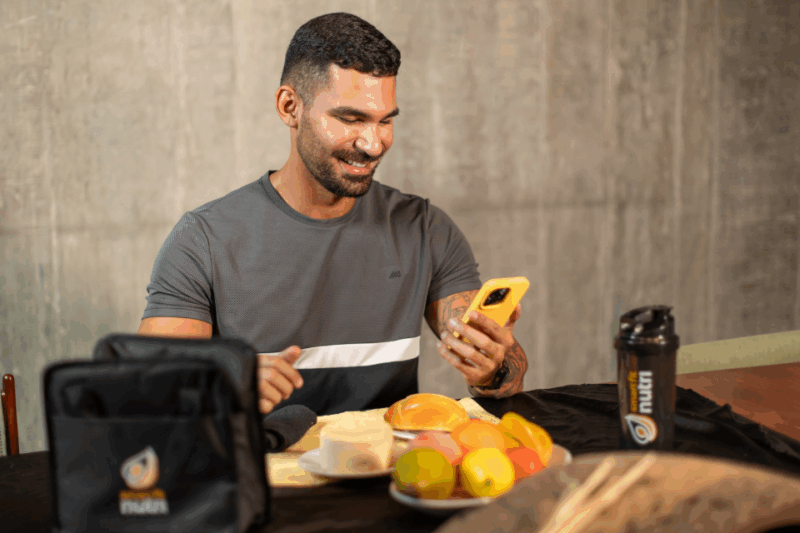 pessoa mexendo no celular com pão e frutas a sua frente