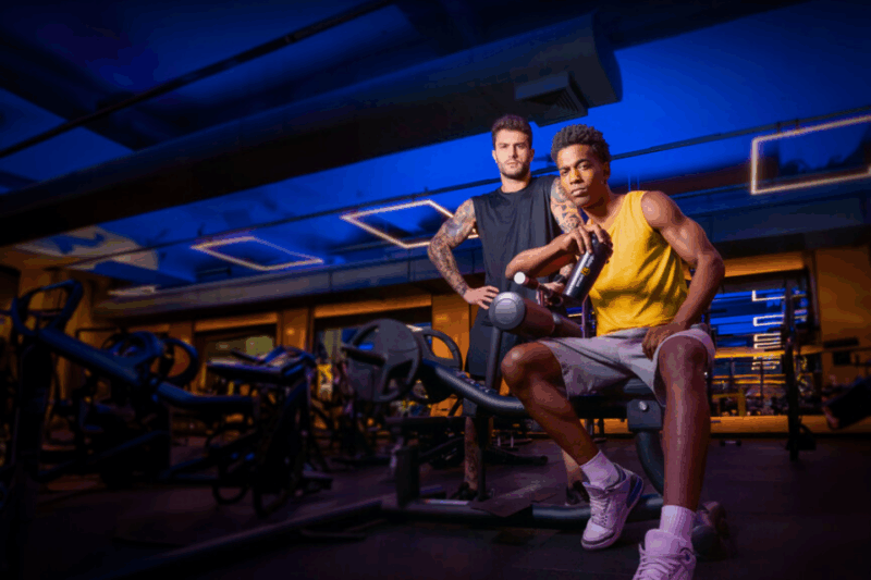 Um homem sentado e outro em pé posando em uma academia da smart fit.