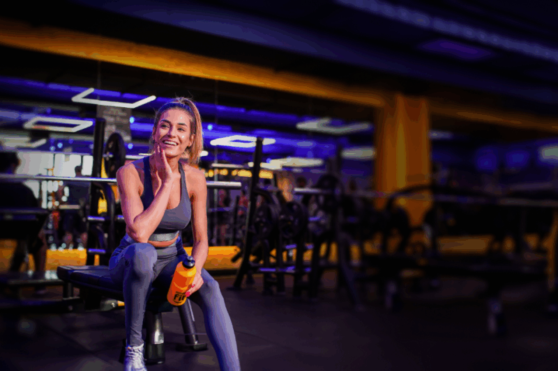 Mulher sentada no banco de uma academia smart fit.