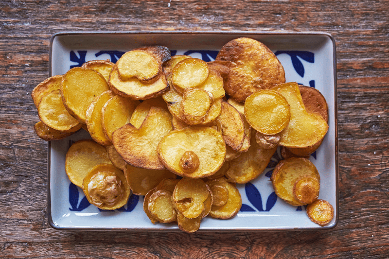 Prato branco e azul cheio de chips de batata doce frita sobre mesa de madeira
