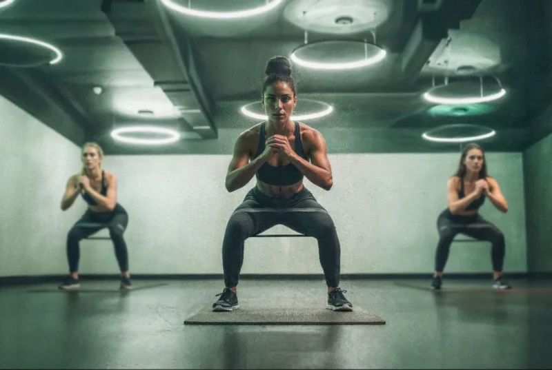 Três mulheres realizando agachamentos em academia moderna