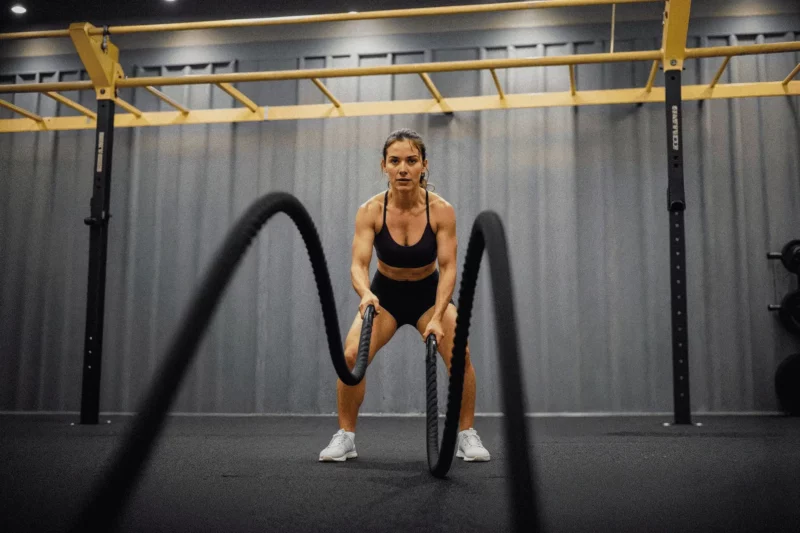 Mulher treinando com cordas de batalha na academia