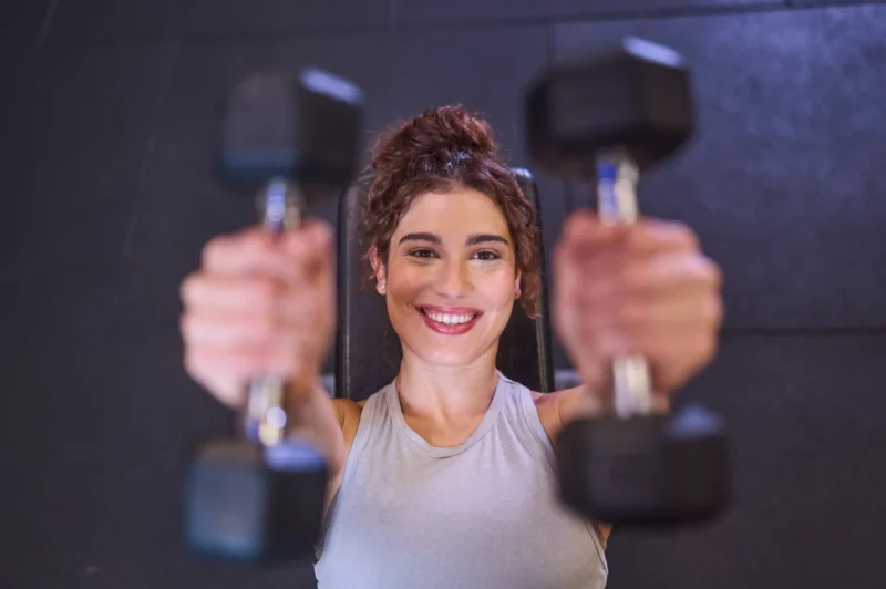 Mulher sorrindo segurando pesos na academia