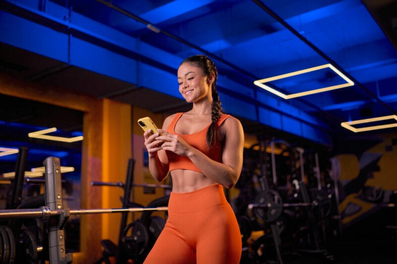 Mulher sorridente em academia usando celular
