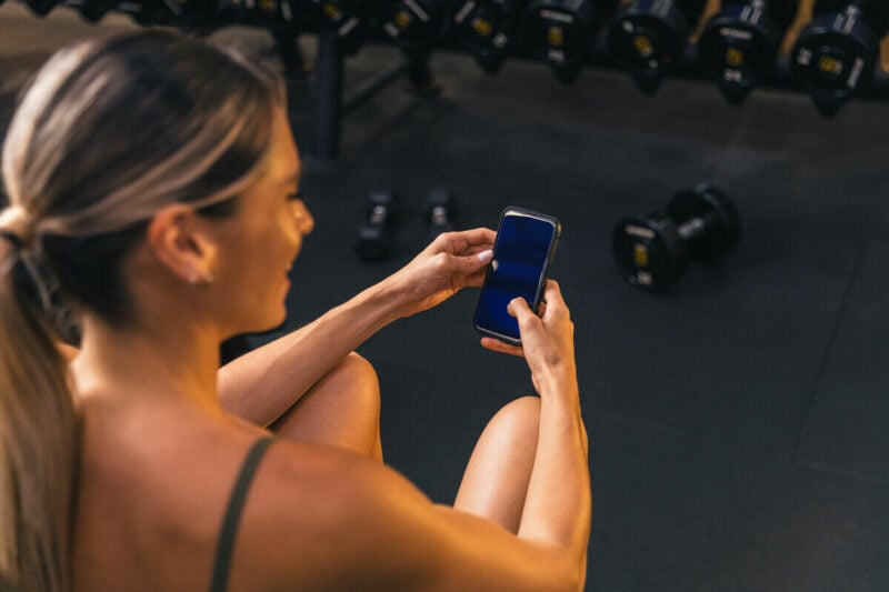 Mulher usando celular na academia, descansando.